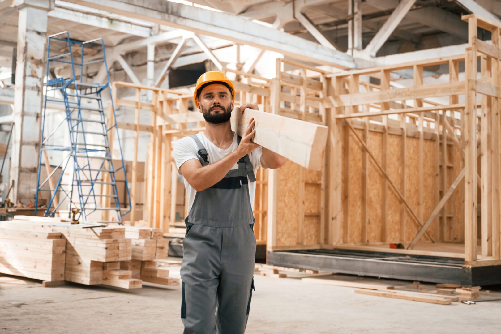 Construction worker carrying wooden plank indoors.